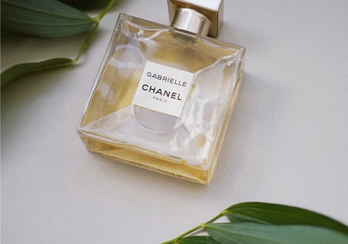 picture of Gabrielle Essence Eau De Parfum laying on its back with green leafs in the background
